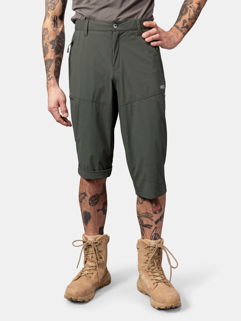 Henkilö, jolla on Halti Pallas Cool X-stretch Caprit, harmaa paita, ruskehtavat saappaat ja tatuoidut kädet ja jalat.