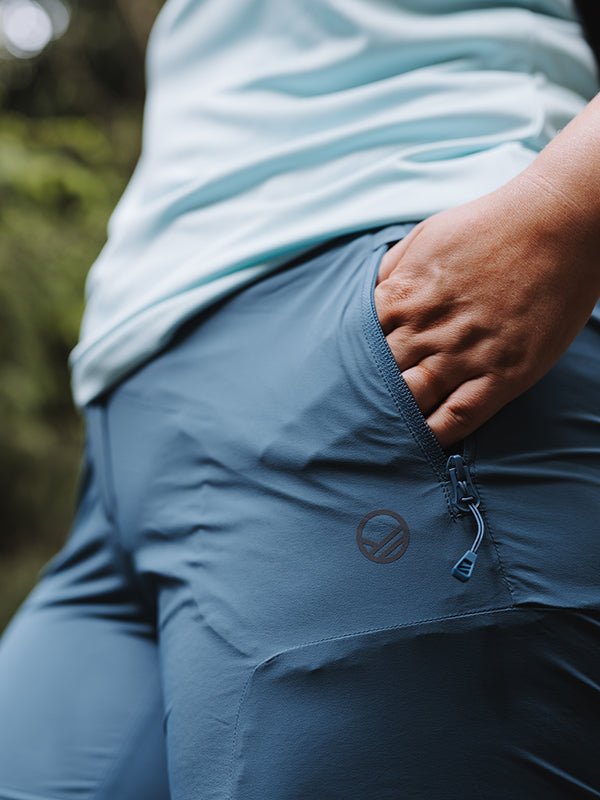 Henkilö, jolla on yllään Halti Pallas Cool X-stretch Caprit Naisten Plus -takit ja vaaleansininen paita, käsi vetoketjullisessa taskussa ulkona.