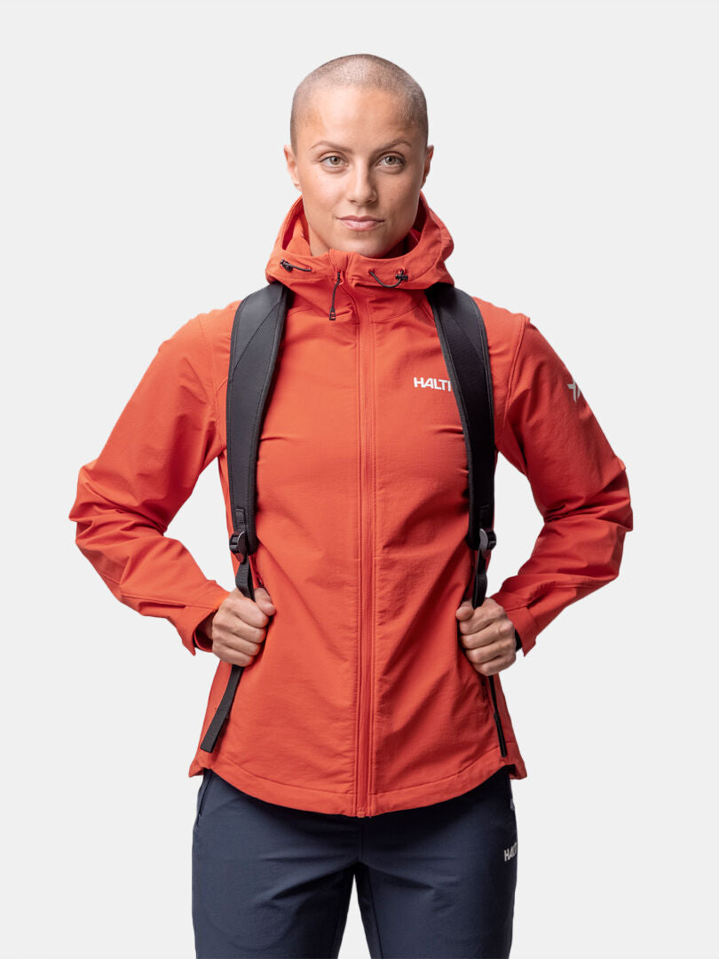 Henkilö, jolla on ajeltu pää, Halti Finholma X-stretch Takki Naisten ja reppu selässä, kasvot menosuuntaan valkoisella pohjalla.