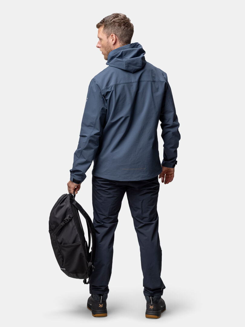 Halti Finholma X-stretch Takki -asuun pukeutunut mies seisoo tummissa housuissa ja pitää mustaa reppua vasemmassa kädessään.