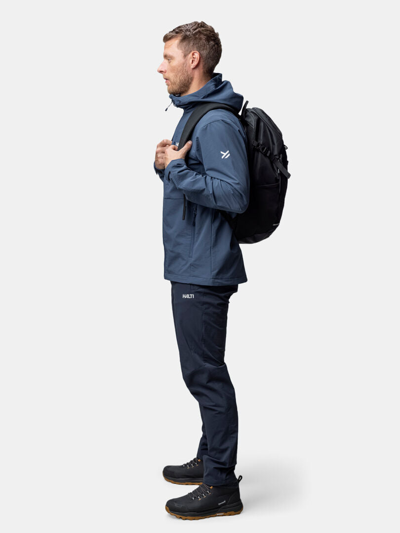 Halti Finholma X-stretch Takki Miesten ja housuihin pukeutunut mies seisoo profiilissa mustan repun ja kenkien kanssa.