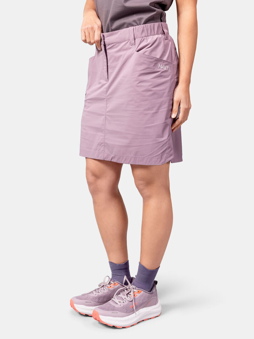Jollakin on yllään vaaleanvioletti Halti Pallas Cool Shortsihame Naisten, yhteensopivat lenkkarit, violetit sukat ja harmaa paita.