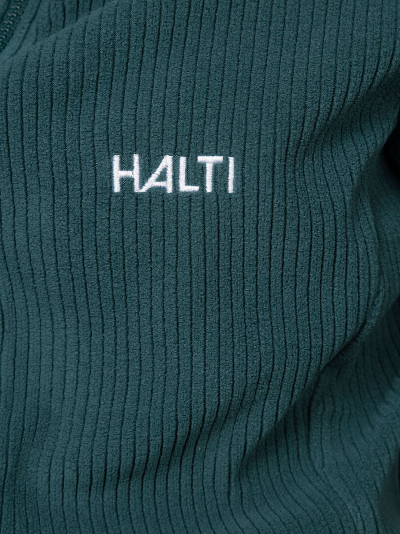 Lähikuva vihreästä, uurrettua Loito 3-in-1 DX Takki Naisten -kankaasta, johon on brodeerattu valkoisella langalla teksti ”Halti”.