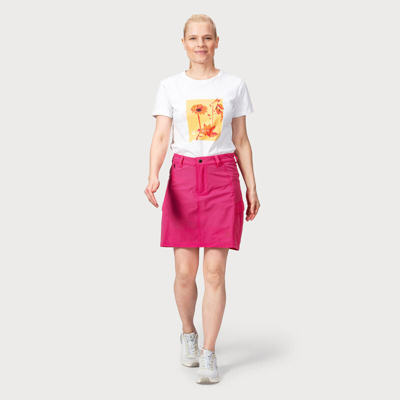 Nainen Halti Reissu Naisten Stretch -shortseissa ja valkoisessa graafisessa t-paidassa kävelee vaaleaa taustaa vasten.