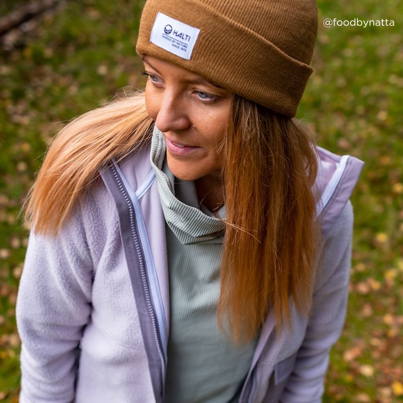 Ruskeassa Halti Laus Pipossa oleva henkilö seisoo ruohikkoisella maalla, jossa on hajallaan lehtiä, ja katsoo sivulle.