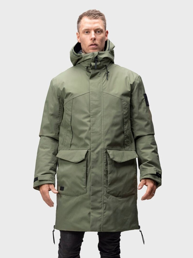 Halti Bergga DrymaxX Talvitakki Miesten henkilö seisoo kasvot menosuuntaan vaaleaa taustaa vasten.