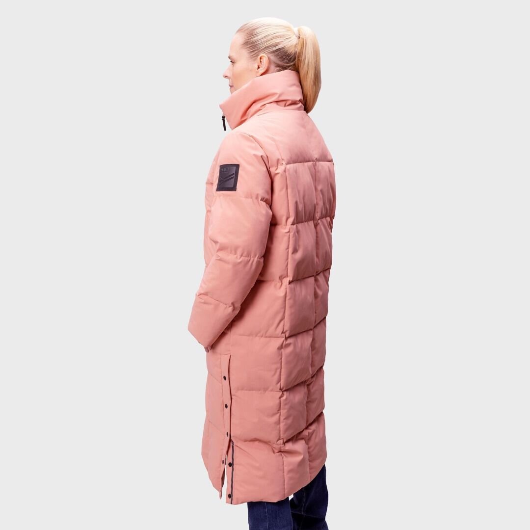 Vaaleanpunaiseen Halti Penger Talvitakki Naisten takkiin ja Microtherm® THERMOFILL -liinaan pukeutunut nainen seisoo sivuttain harmaata taustaa vasten.