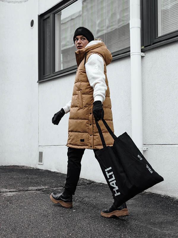 Henkilö, jolla on ruskehtava Halti Penger -toppaliivi, valkoinen huppari ja musta pipo, kantaa suurta mustaa Halti-kantolaukkua.