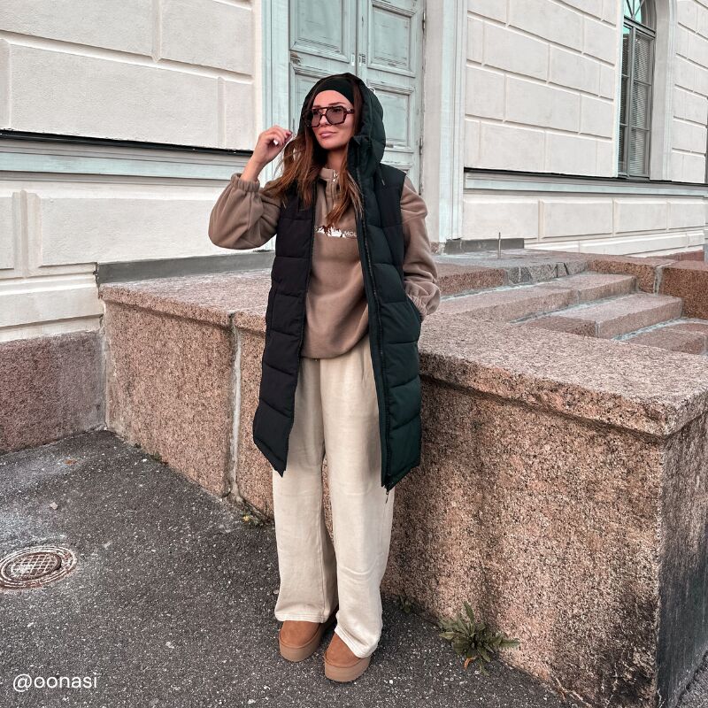 Haltin Penger Toppaliivi Naisten ja beigeihin housuihin pukeutunut nainen seisoo ulkona kiviportaiden luona, liivit estävät tuulenvireen.