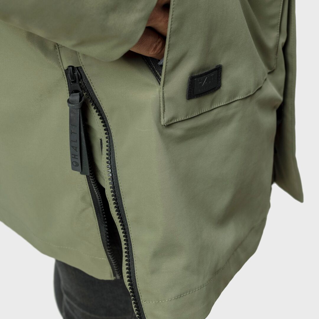 Lähikuva henkilöstä oliivinvihreässä Halti Synkas 3in1 DrymaxX Parka Miesten -takissa, jossa on CHÁIT-merkkinen vetoketjun vedin.