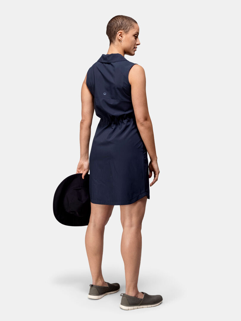 Joku Halti Chipper X-stretch Mekko Naisten paidassa ja harmaissa kengissä seisoo kasvot poispäin ja pitelee mustaa hattua vasemmalla kädellä.