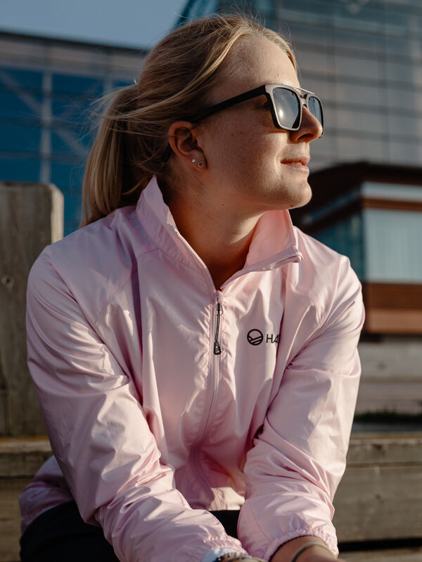 Halti Saime Tuulitakki Naisten ja aurinkolaseihin pukeutunut henkilö istuu ulkona auringonpaisteessa ja katsoo kauas.