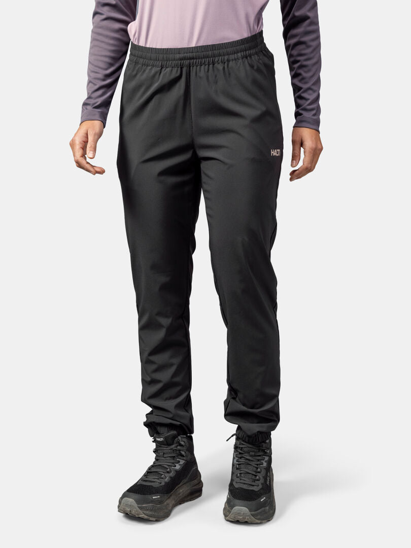 Henkilöllä on yllään mustat Halti Grets Joggersit Naisten, pitkähihainen paita ja vaelluskengät tavallista taustaa vasten.