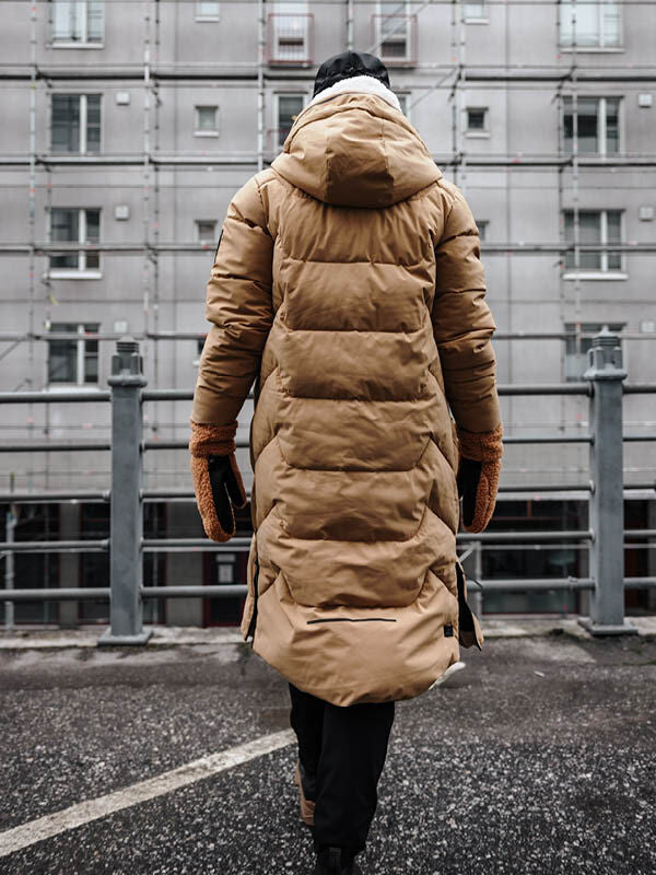 Halti Brahe Puffer Pitkä Talvitakki Naisten henkilö kävelee märällä jalkakäytävällä kerrostalon luona.