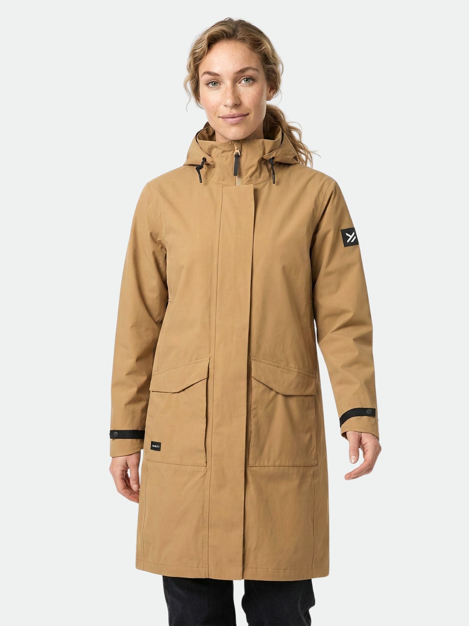 Henkilöllä on yllään ruskehtava Halti Tokoi II DX Parkatakki Naisten, jossa on suuret etutaskut, vaaleaa taustaa vasten.