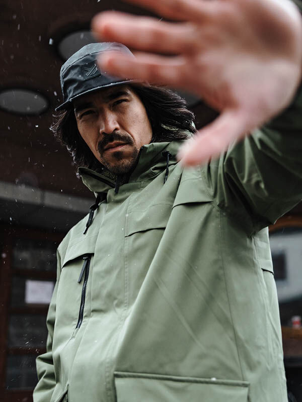 Mies, jolla on Halti Tokoi II DX Parkatakki Miesten ja musta hattu, pitää kättään ylhäällä ja peittää osittain kasvonsa.