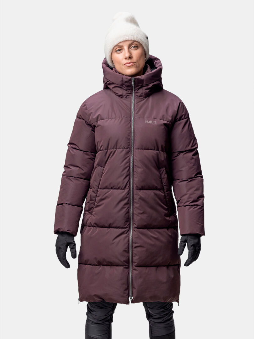 Henkilöllä on yllään Halti Sammal Topattu Parkatakki Naisten, mustat hanskat ja housut sekä valkoinen pipo.