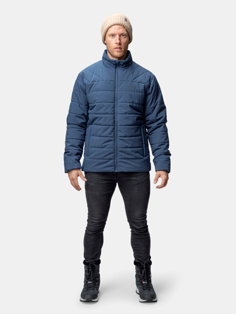 Henkilöllä on päällään sininen Halti Haapa Kevyttoppatakki Miesten, mustat housut ja saappaat sekä beige neulottu pipo, kasvot eteenpäin.