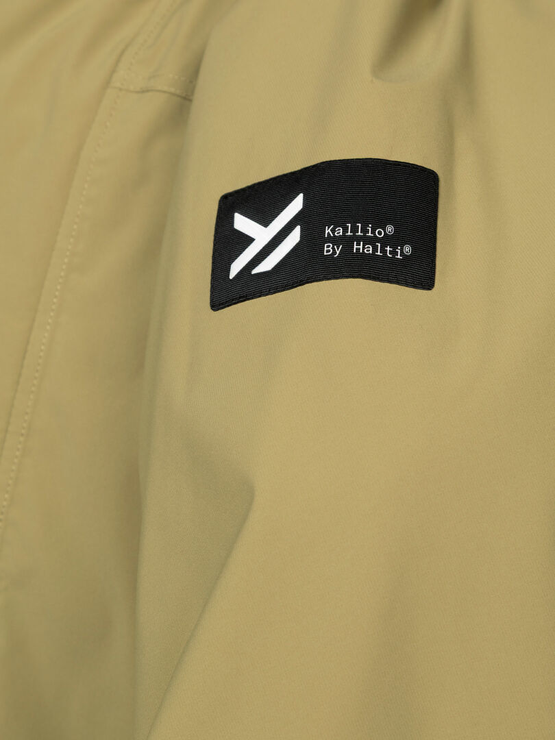 Lähikuva khakinvärisestä Kortteli DX Parka Miesten -kankaasta, jossa on musta Halti-merkki ja valkoinen abstrakti logo.