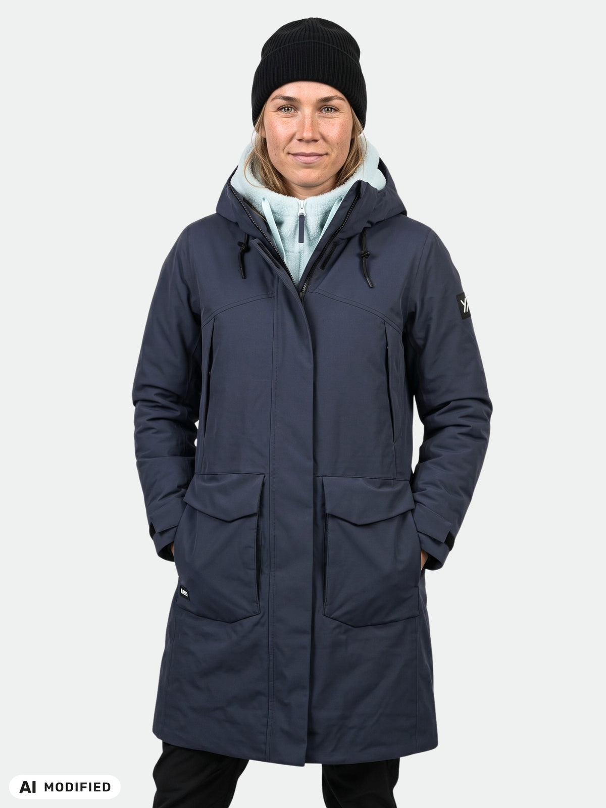 Henkilö, jolla on yllään Halti Kallio DX Parka Naisten (navy) -takki, vaalea huppari ja musta pipo; kädet taskussa, katse eteenpäin suunnattuna.