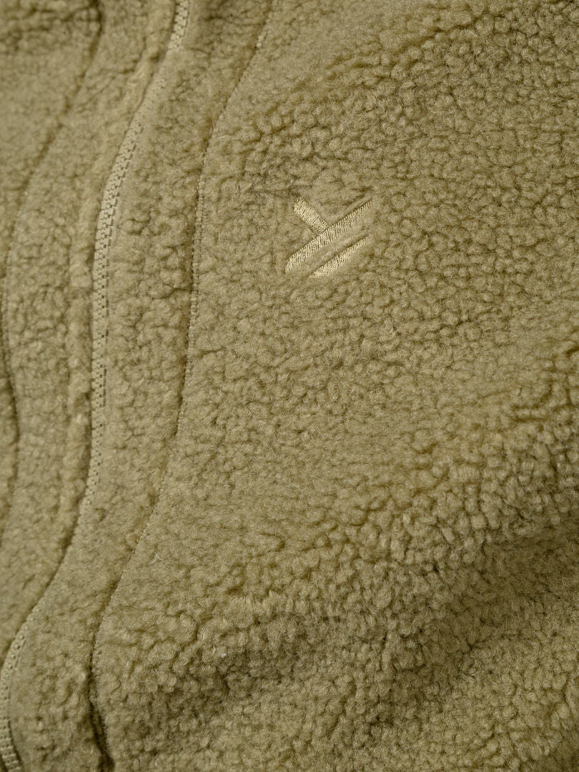 Lähikuva Halti Lykky Fleece Liivi Unisex -tuotteesta vaalean oliivinvihreänä; kuvassa näkyy kierrätettyä polyesteriä, vetoketju ja ommeltu logo.