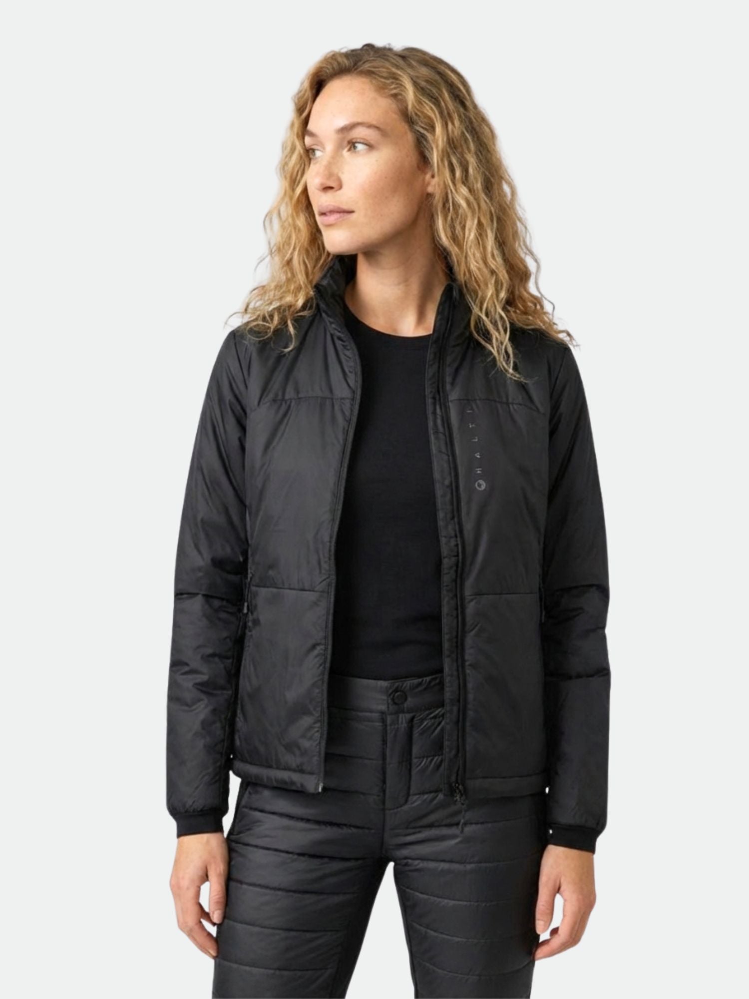 Mustaan Halti Neon Kevytvanutakki Naiseen pukeutunut nainen seisoo hieman vasemmalla tavallista vaaleaa taustaa vasten.