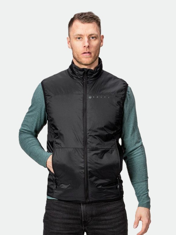 Miehellä on yllään Halti Neon Primaloft Toppaliivi Miesten teal paidan päällä, seisoo eteenpäin toinen käsi taskussaan.