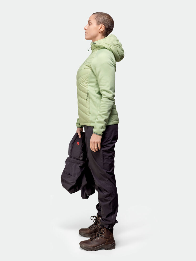 Henkilöllä vaaleanvihreä Halti Huippu Hybrid Untuvatakki, mustat housut, ruskeat saappaat, kädessä musta takki.