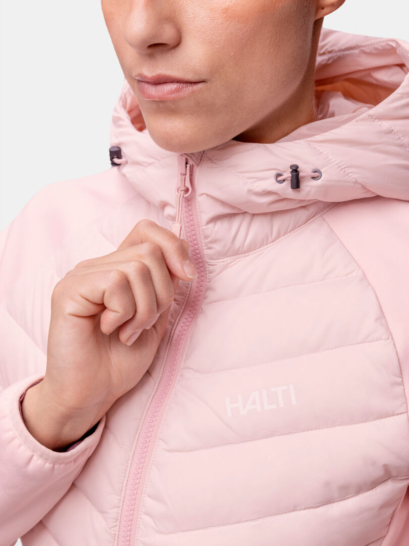 Nainen vetoketjulla kiinni vaaleanpunaisessa Halti Huippu Hybrid Untuvatakissa, jossa on huppu, näytetään olkapäistä nenään.
