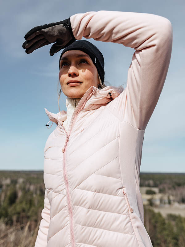 Henkilö ulkona vaaleanpunaisessa Halti Huippu Hybrid Untuvatakki Naisten ja mustissa hanskoissa katselee kaukaisuuteen.