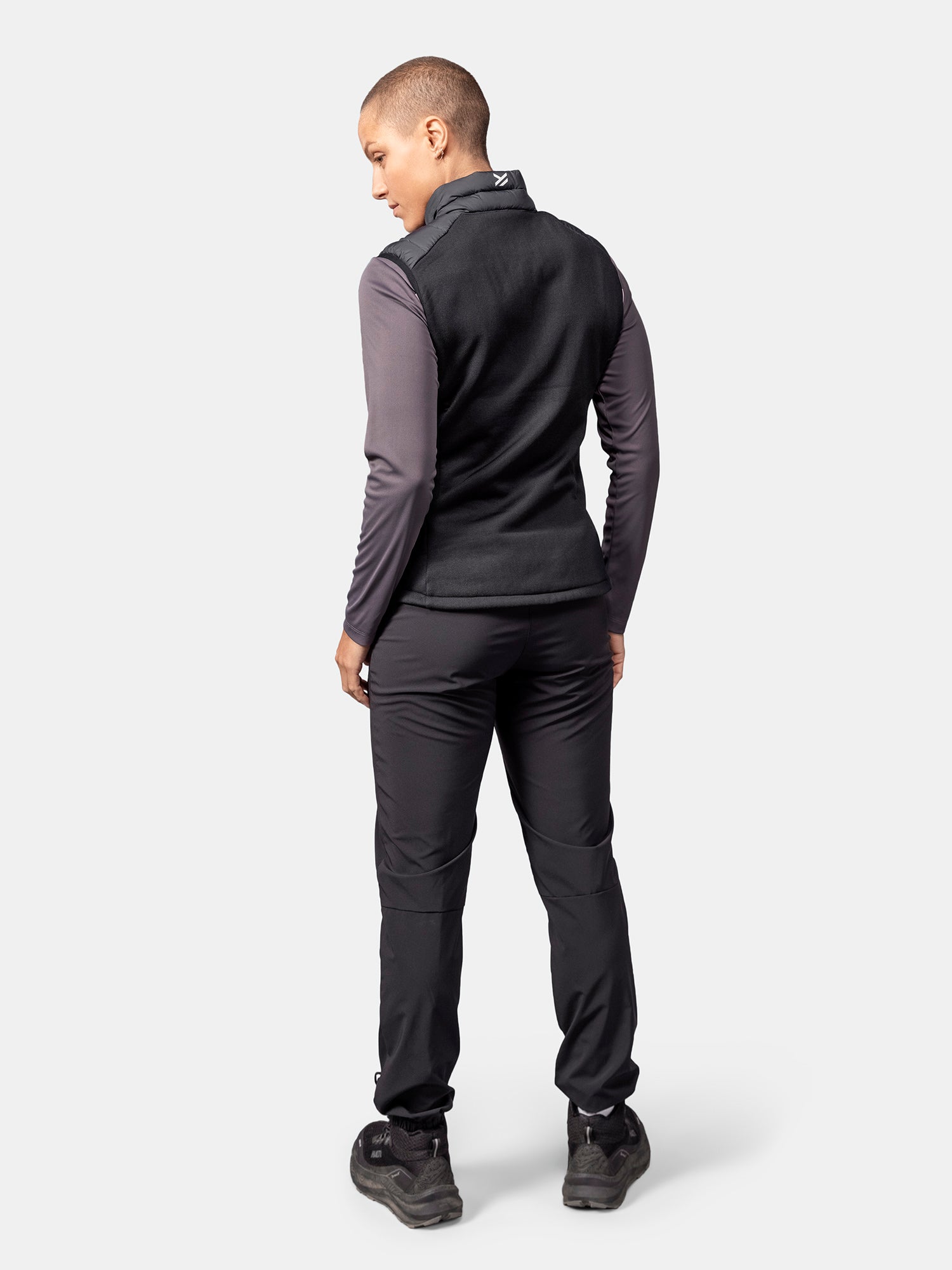 Henkilöllä on yllään musta Halti Huippu Hybrid Untuvaliivi Naisten liivi, harmaa pitkähihainen paita, mustat housut, selkä kameraan päin.