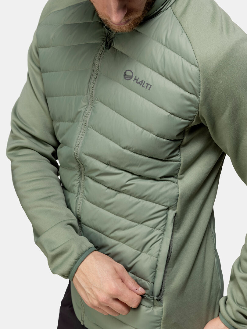 Vaaleanvihreään Halti Huippu Hybrid Untuvatakki -takkiin pukeutunut mies vetää vetoketjun sivutaskusta alaspäin katsoen.