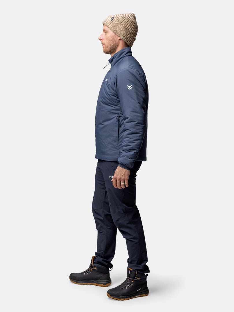 Siniseen Halti Haave Primaloft Takki Miesten ja ruskeisiin saappaisiin pukeutunut mies seisoo profiilissa valkoista taustaa vasten.