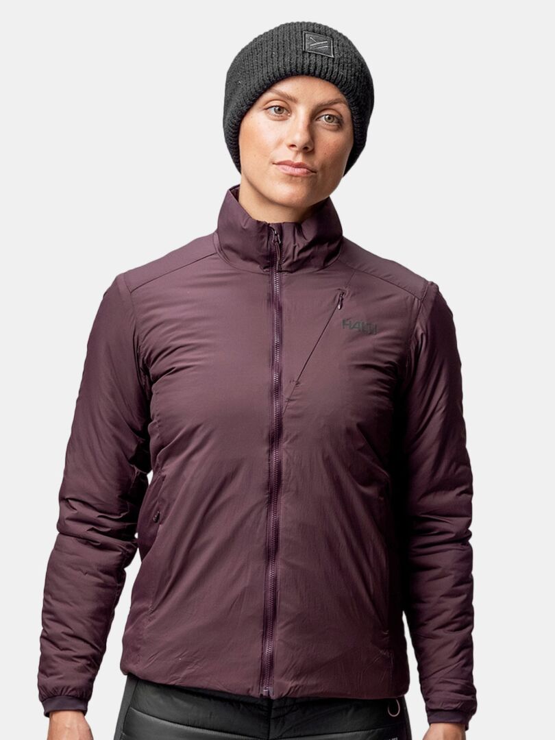 Henkilö, jolla on yllään tumma Halti Huurre Panta ja ruskeankeltainen vetoketjullinen takki, seisoo kameraan päin tavallista taustaa vasten.