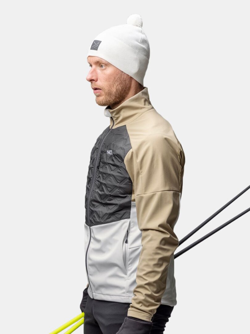 Halti Pilke Pipo -asuinen mies seisoo profiilissa, suksisauvat olkapäänsä yli pitäen, taustan ollessa tavallinen.