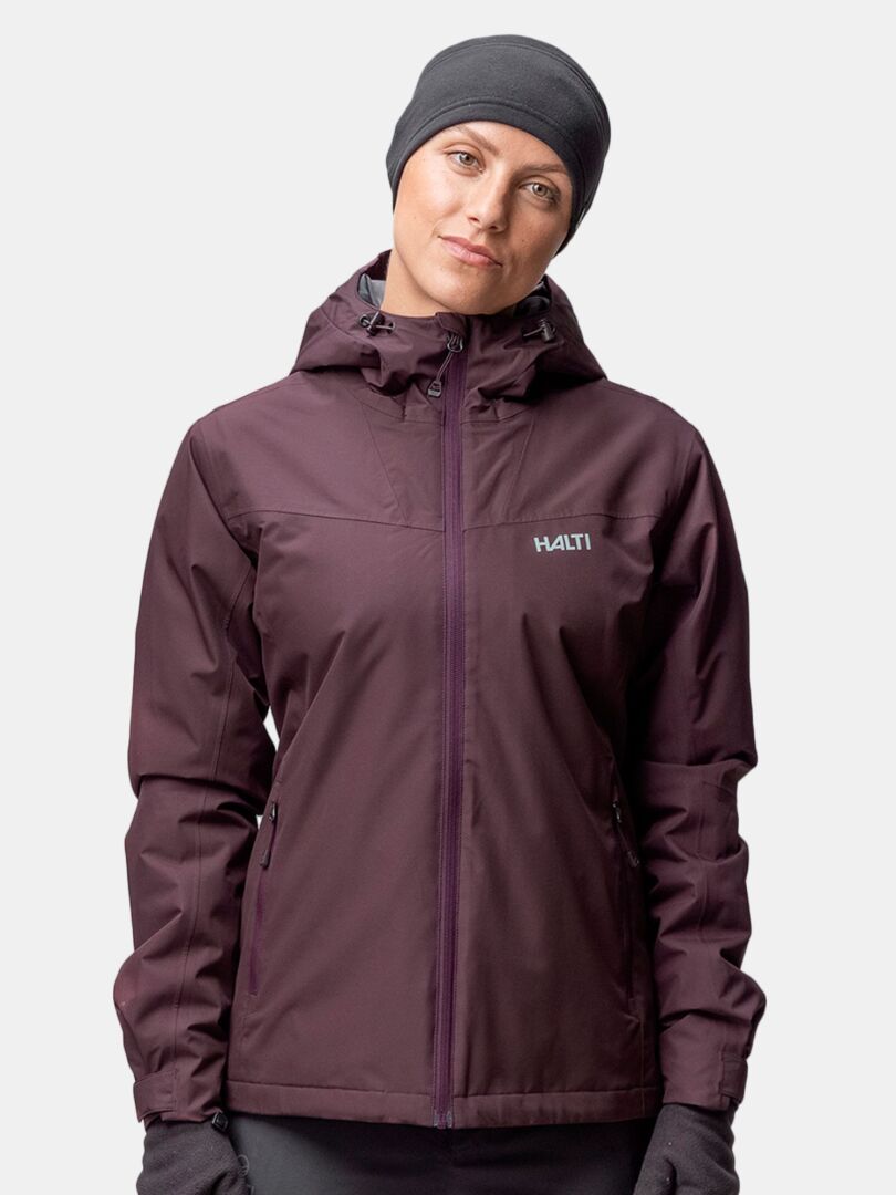 Henkilö, jolla on tummanvioletti hupullinen takki ja Halti Trone Fleece Panta, valmiina talviaktiviteetteihin vaaleaa taustaa vasten.