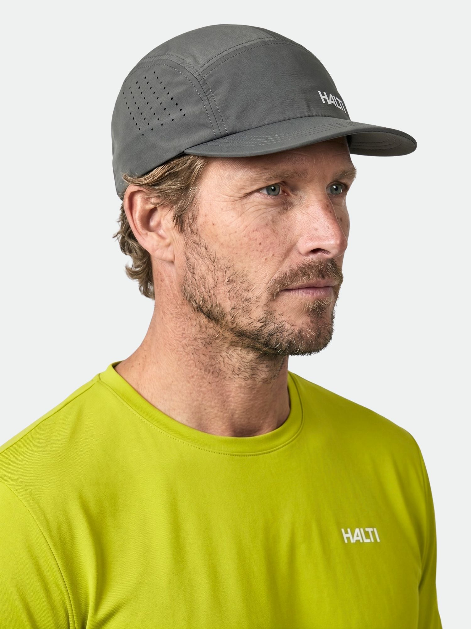 Luovi Lippis ja kirkkaan kelta-vihreä Halti-paita päällään mies katsoo oikealle vaaleaa taustaa vasten.