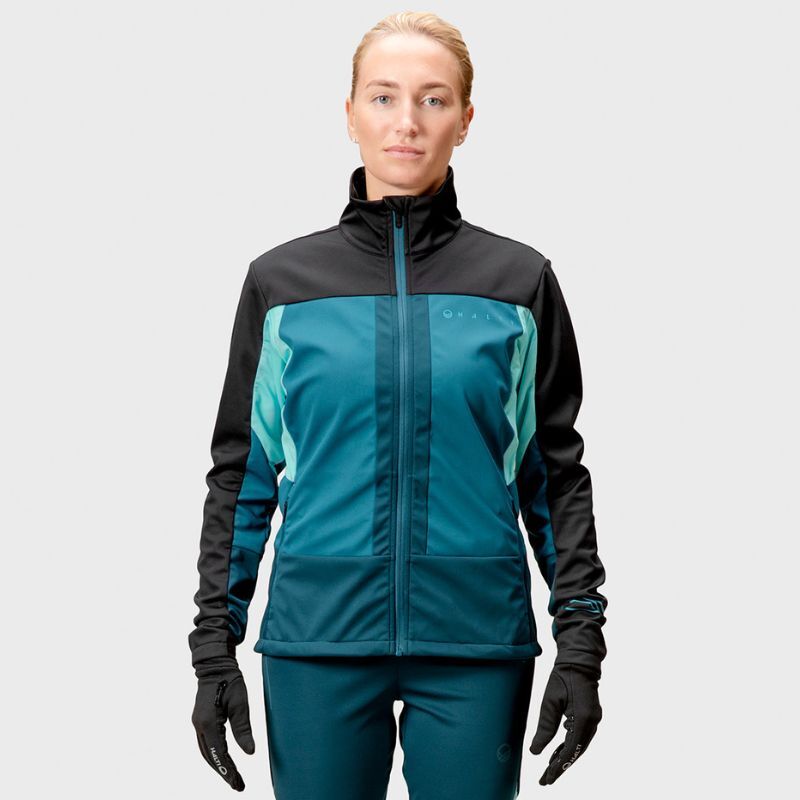 Henkilö katsoo eteenpäin ja käyttää Stormwall®-materiaalista valmistettua Halti Vinha Hiihtotakki Naisten takkia sinivihreänä ja mustana.