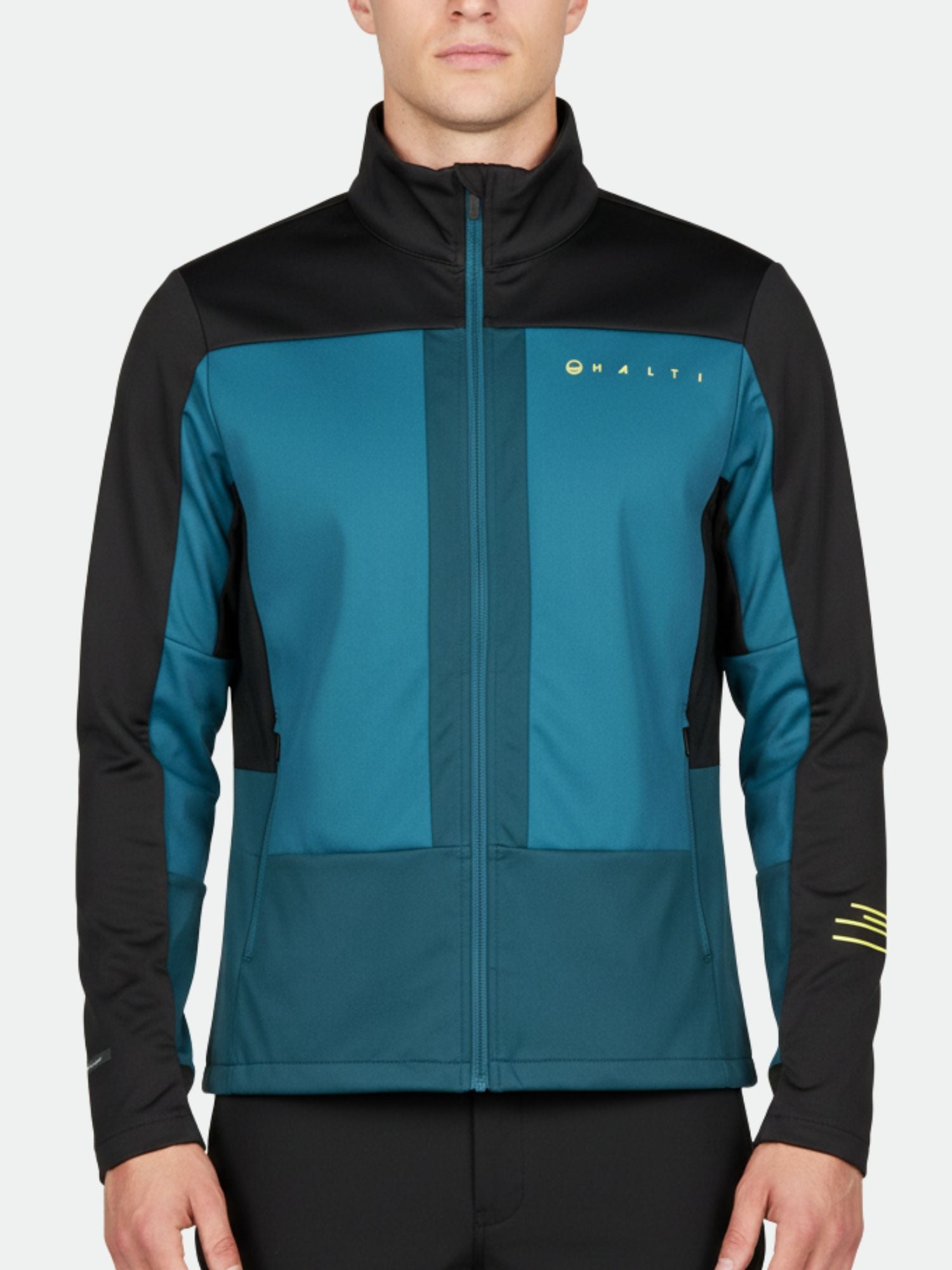 Miehellä on yllään Halti Vinha Hiihtotakki Miesten, tiilenpunainen ja musta vetoketjullinen takki, jossa on pitkät hihat ja logo rinnassa.