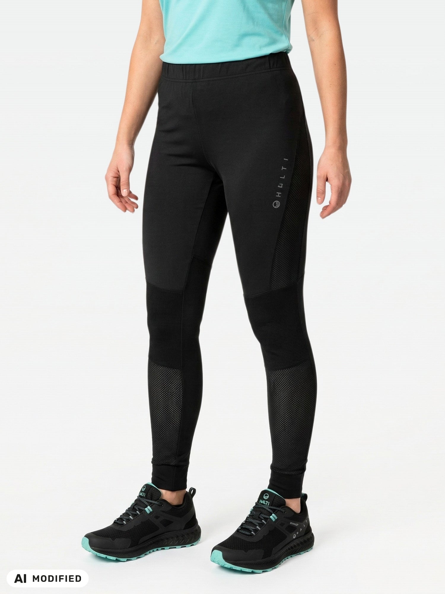 Henkilö on pukeutunut Halti Tracksin Naisten Seamless Trikoot -leggingsiin, turkoosiin paitaan ja mustiin kenkiin yksiväristä taustaa vasten.