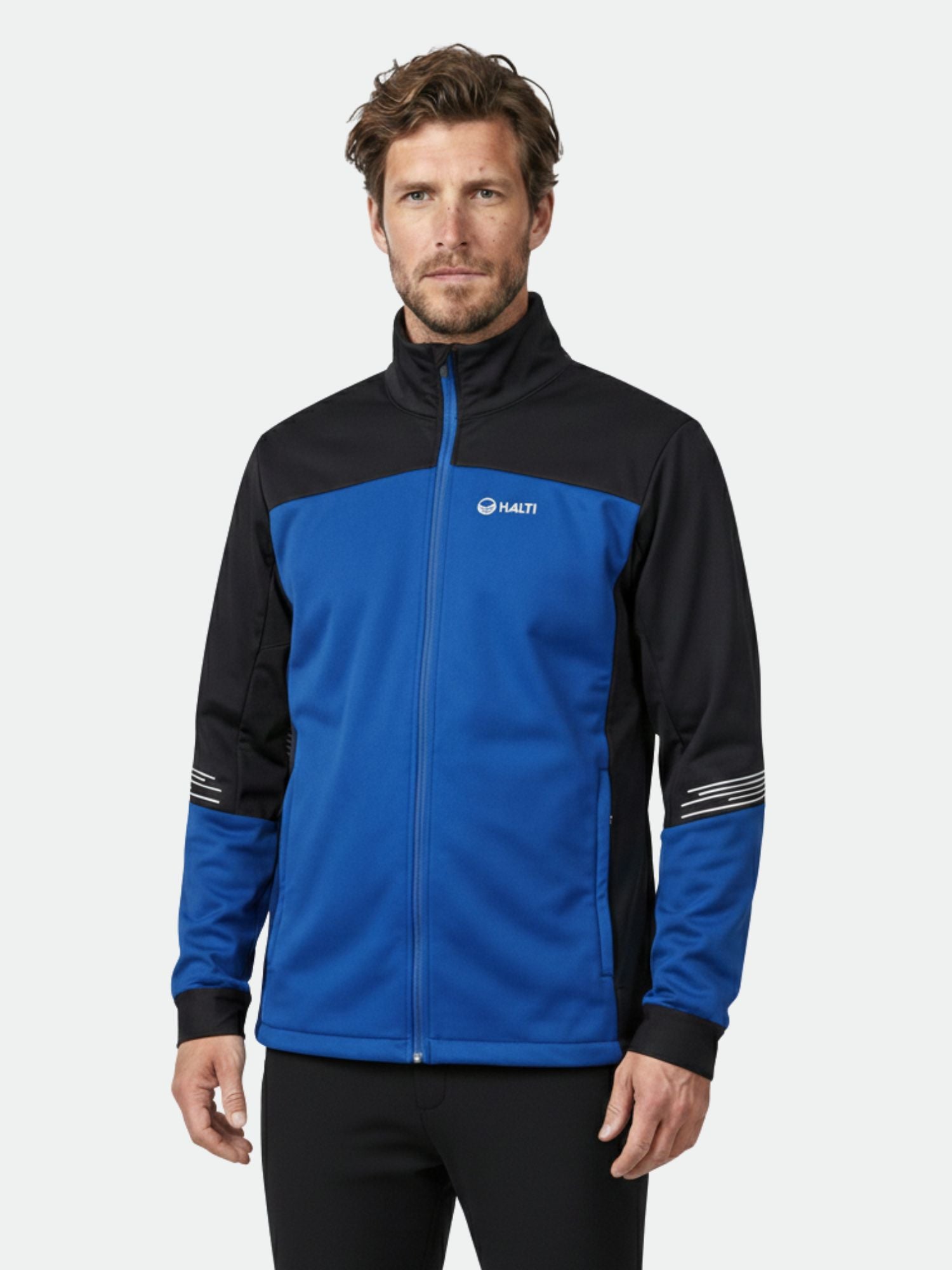 Sinimustaan Halti Siide Hiihtopuku Miesten takkiin Stormwallin kanssa pukeutunut mies seisoo tavallista taustaa vasten.