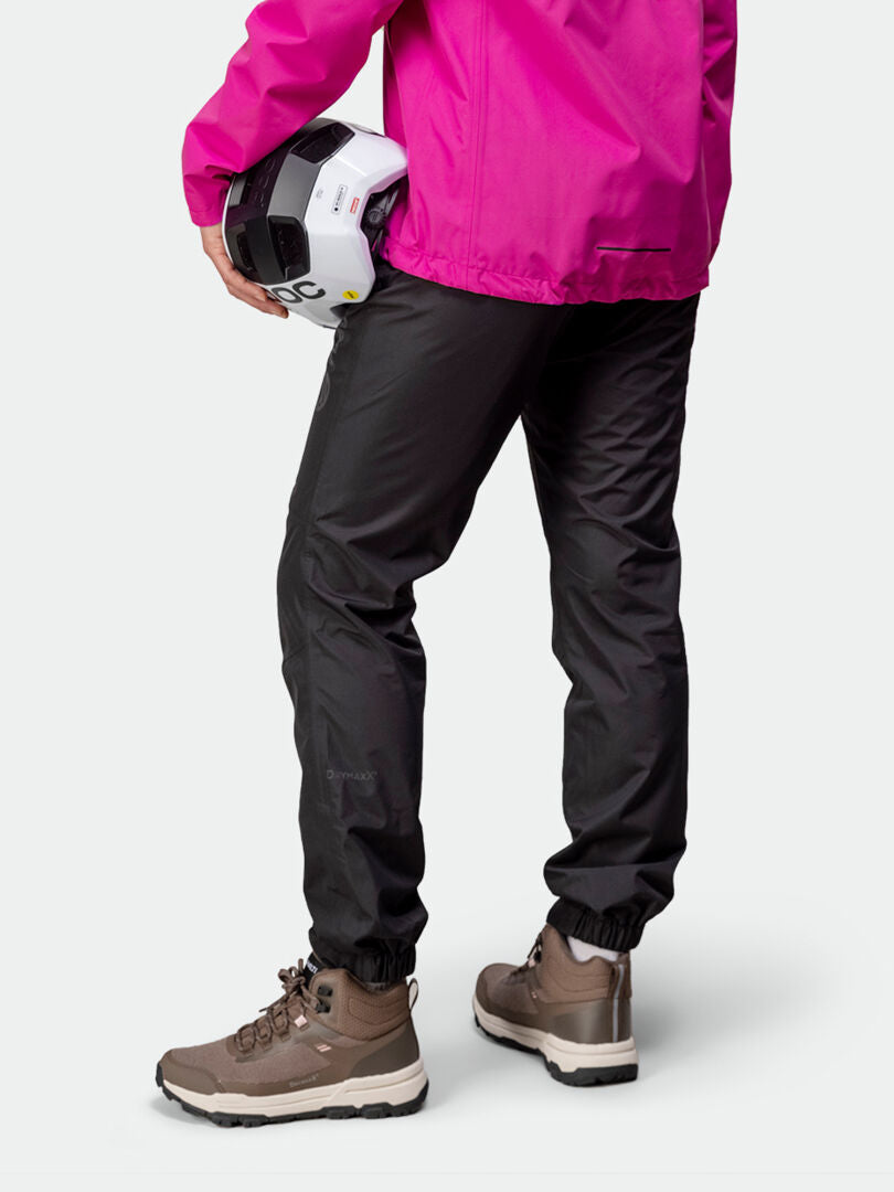 Henkilö Halti Triant DX Pyöräilyhousut Naisten ja ruskeissa saappaissa pitelee valkoista kypärää ja hänellä on yllään vaaleanpunainen takki, kuva takaa.