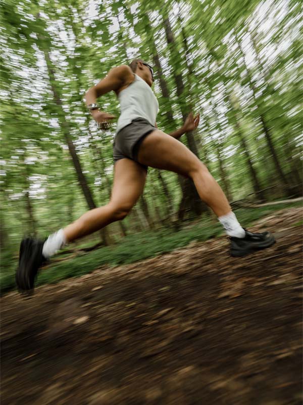 Juoksija Halti Uurto Shortsit Naisten ja tank top treenaa intensiivisesti metsäpolulla, motion blur vangitsee ponnistelun.