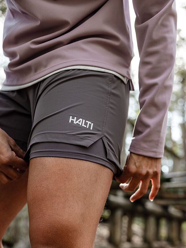 Henkilö, jolla on harmaa Halti Uurto Shortsit Naisten ja violetti pitkähihainen toppi, seisoo ulkona, takana puita.