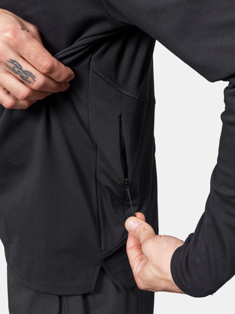 Henkilö avaa mustan Halti Kaltio Treenihuppari Miesten vetoketjullisen sivutaskun, lähikuva käsistä.
