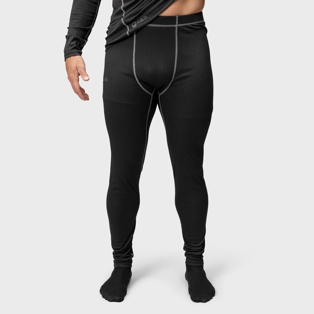 Henkilö mustassa Halti Dual Kerrasto Miesten asussa seisoo vaaleaa taustaa vasten.