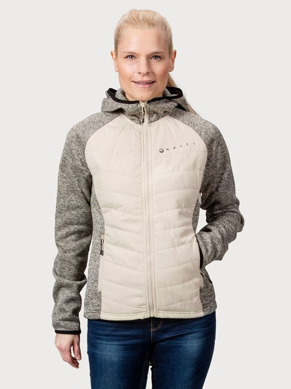 Naisella on yllään Halti Streams Hybrid Välitakki Naisten beige ja harmaa, jossa on etutaskut, tavallista taustaa vasten.