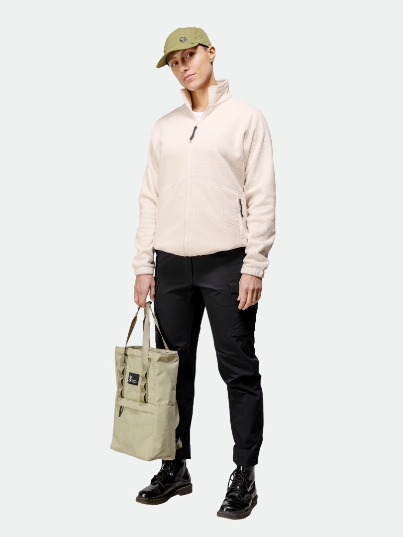 Henkilöllä on yllään Halti Soolo Välitakki Naisten, mustat housut, saappaat, vihreä lippis ja siihen sopiva vihreä laukku.