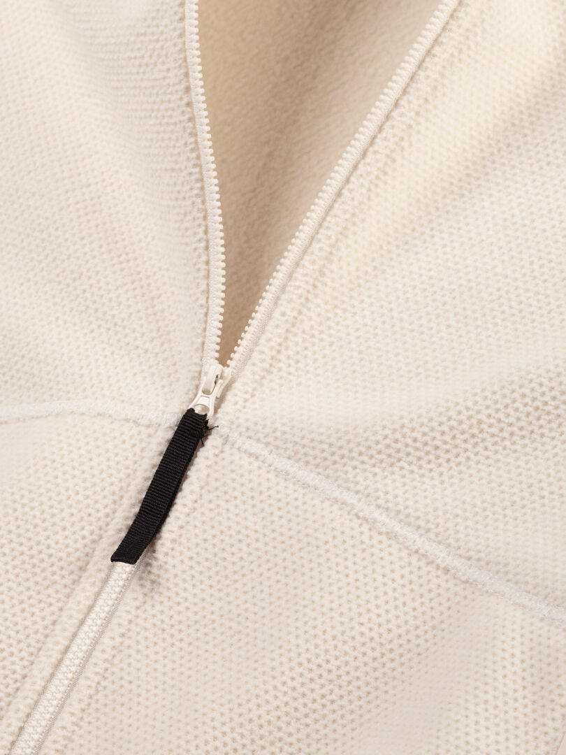 Lähikuva Halti Soolo Välitakki Naisten -takista: valkoinen fleecetakki, jossa on osittain auki vetoketju ja musta vetoketjun vetin.