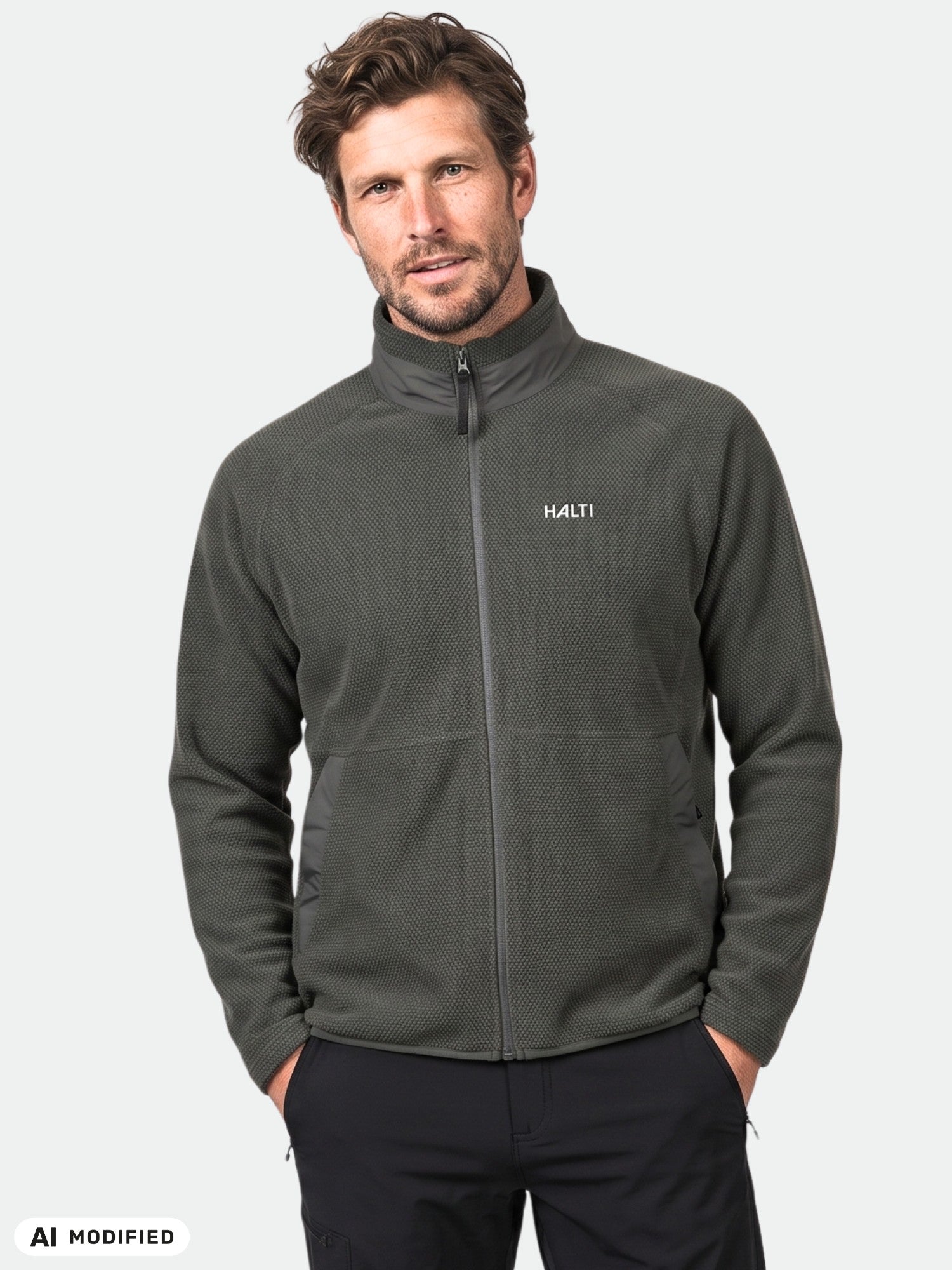 Mies, jolla on yllään tumma Halti Soolo Välitakki Miesten -fleece, seisoo kädet taskussa ja katsoo kameraan.